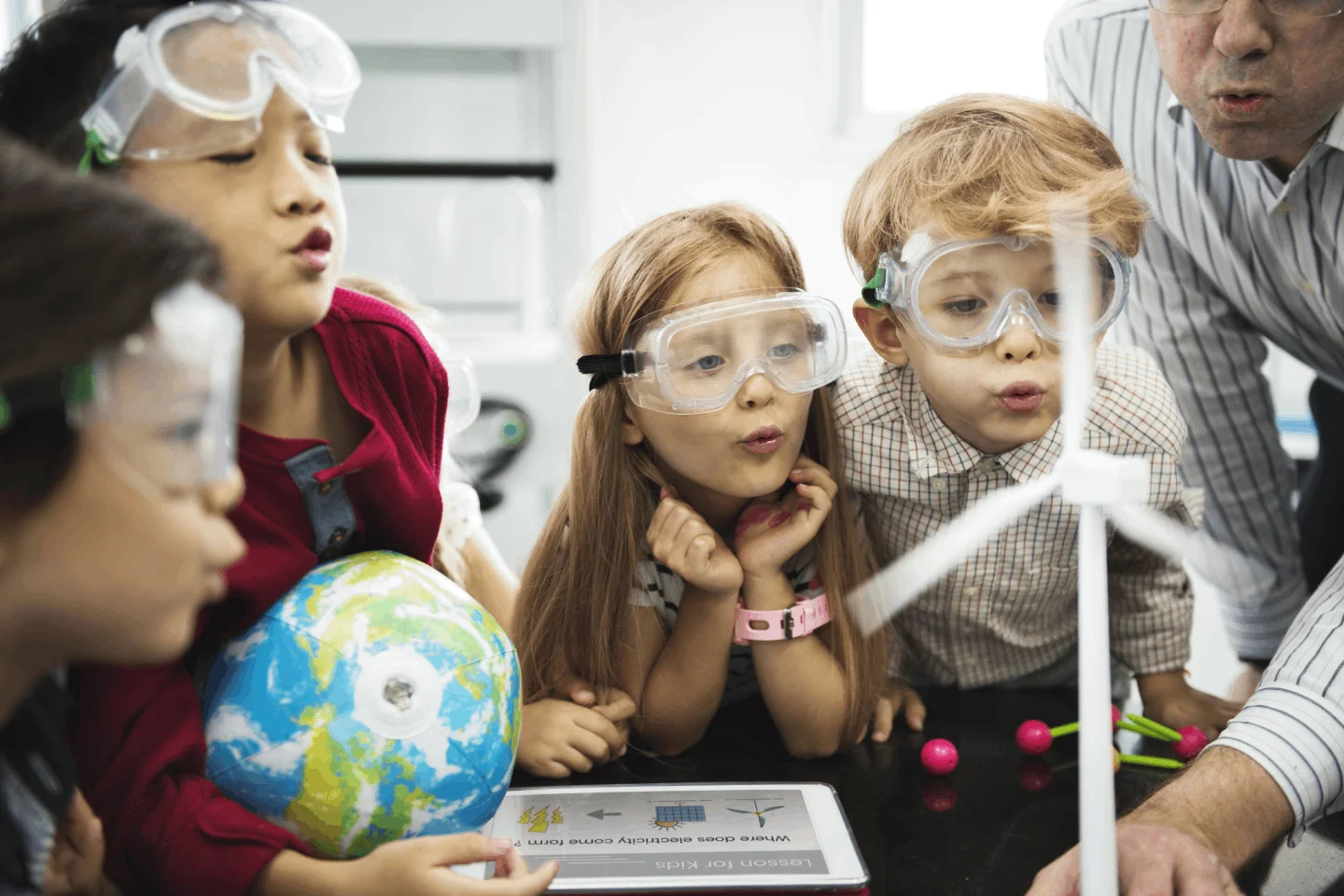 Children in safety goggles watching a science experiment with a globe and a wind turbine model