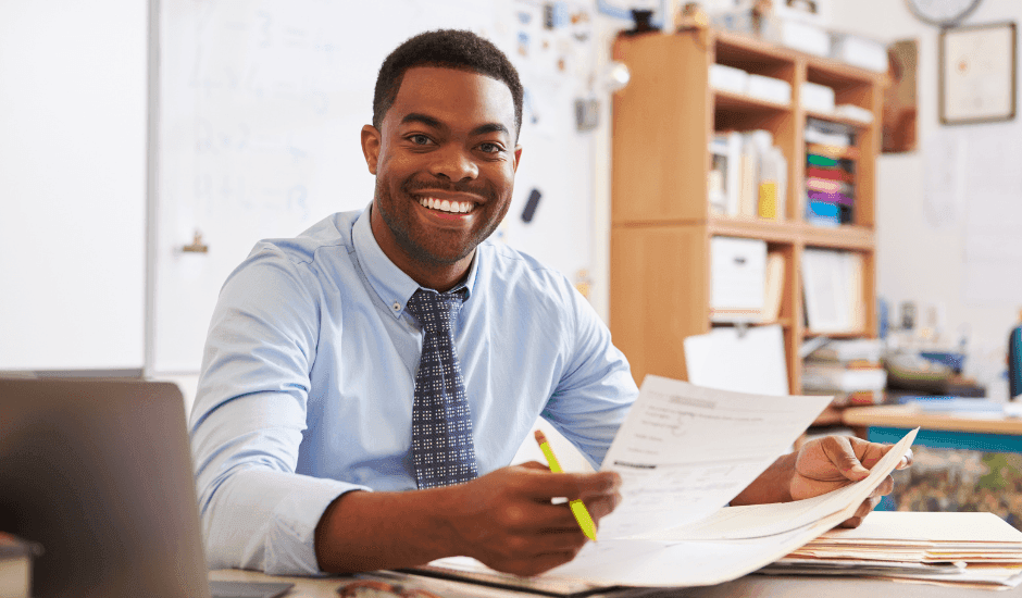 Male teacher smiling at his desk after starting a new teaching job