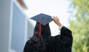 A Newly Qualified Teacher In Graduation Cap And Gown On A University Campus, About To Start Their Ect Induction